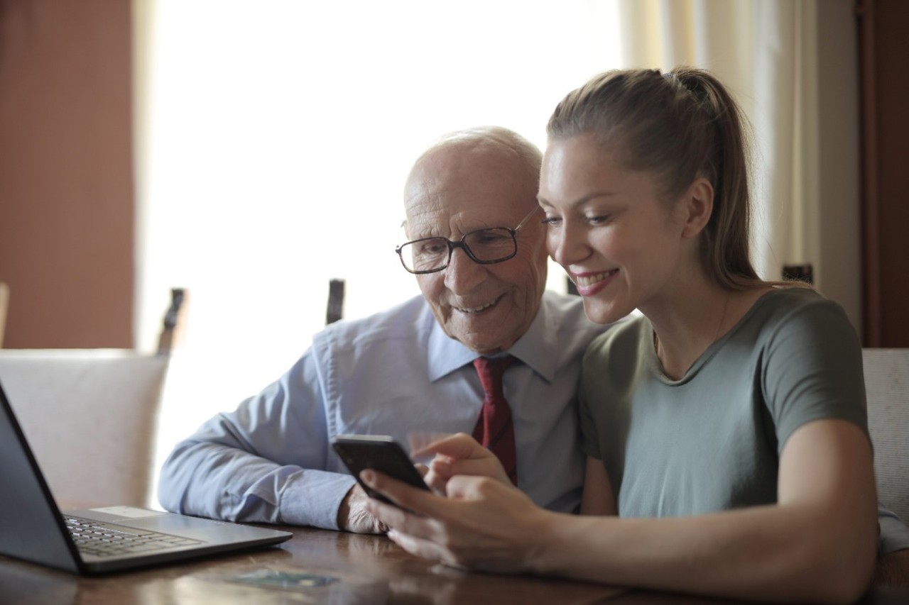 Elderly man being assisted with his phone by a young woman