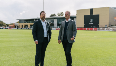 Two men dressed in suits standing on a sports field posing for a photo