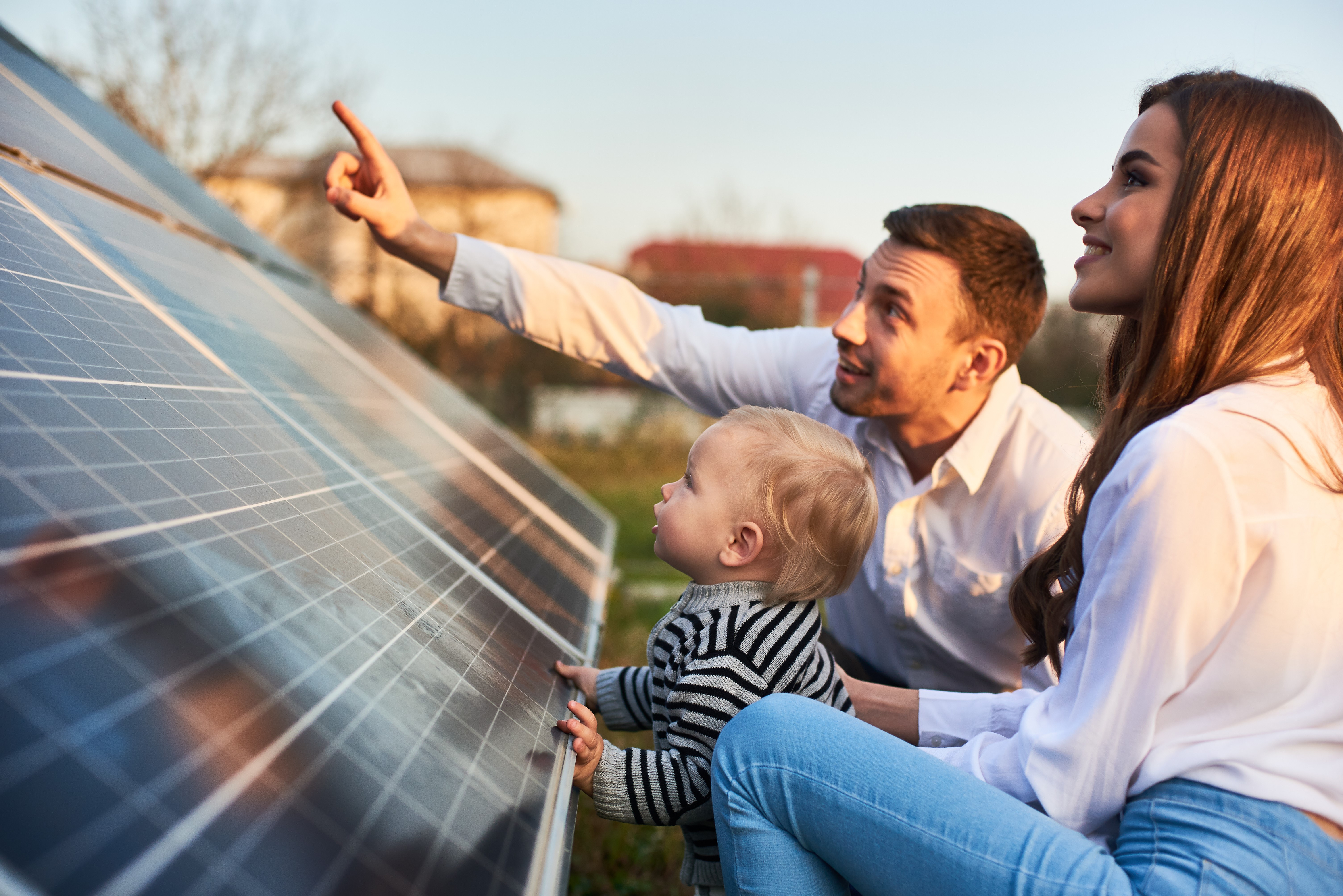 Young family of three crouching in front of a solar panel looking up
