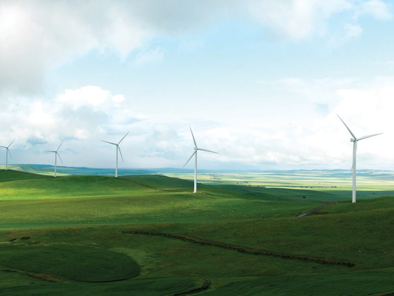 A serene landscape of rolling green hills under a soft blue sky with fluffy clouds, dotted with several white wind turbines. The scene conveys a sense of tranquility and the harnessing of wind energy, illustrating an expansive, rural wind farm.