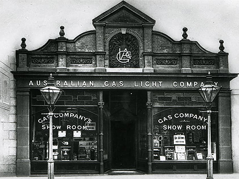 Black and white photo of the Australian Gas Light Company building front with 'GAS COMPANY'S SHOW ROOM' displayed on windows, a street lamp in front.