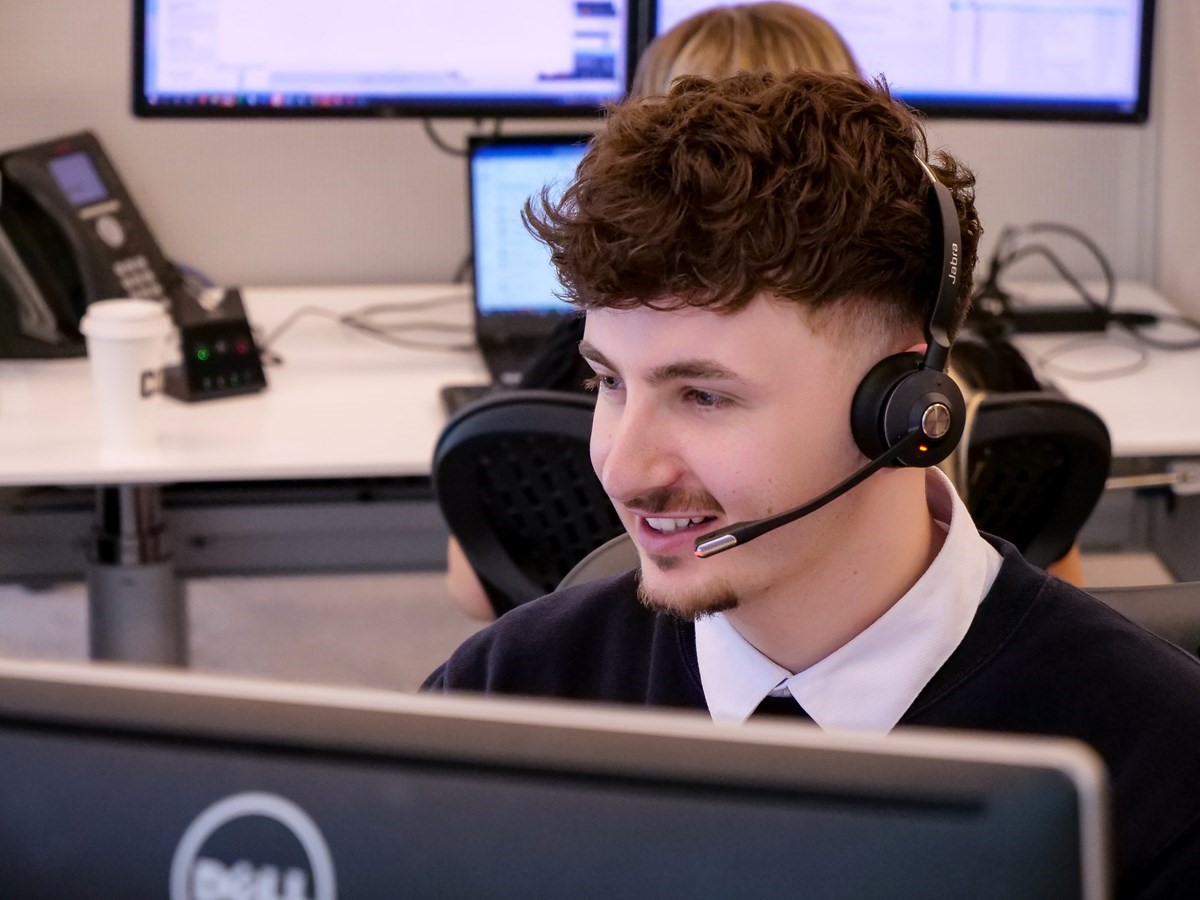 Smiling male customer service representative using a headset while working on computer. 