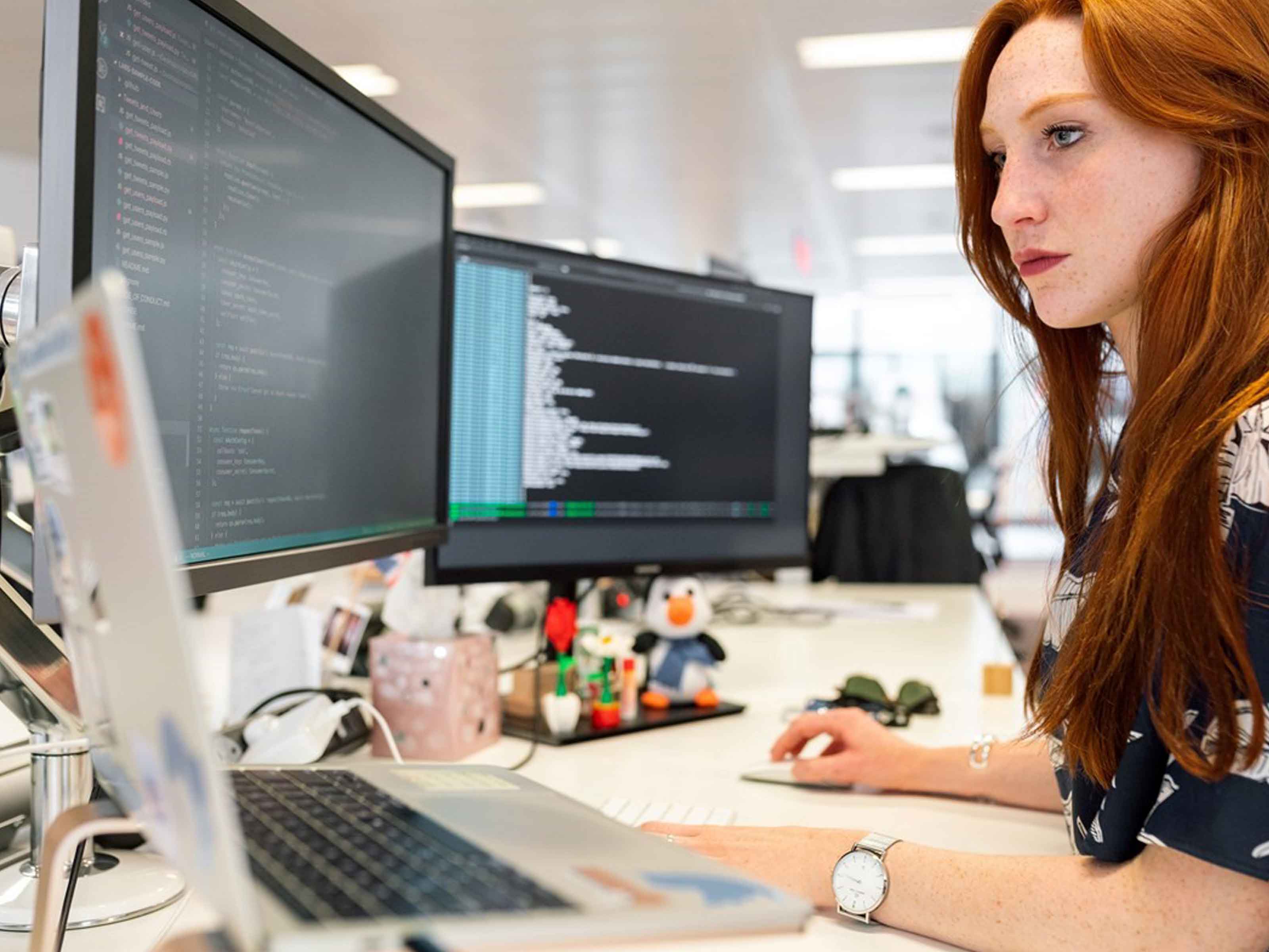 Woman at desk with laptop and two computer screens in front of her