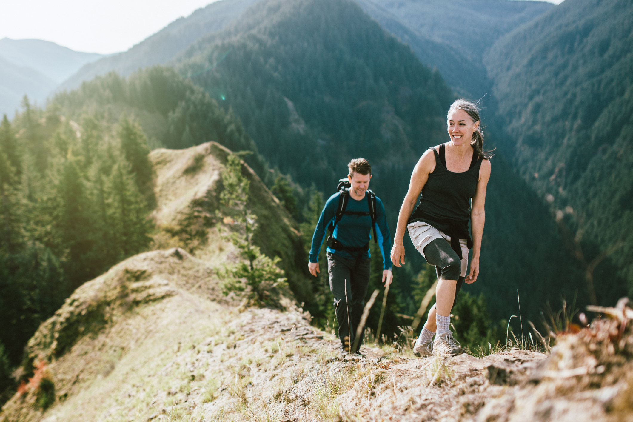 A fit man and woman in their 50's hiking the trail on a mountain ridge.