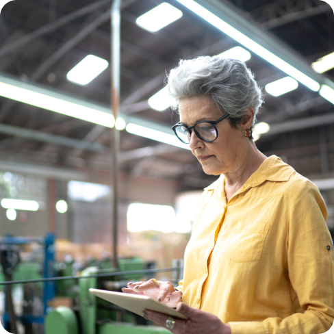 A lady with grey hair standing in an office looking at a tablet in her hands