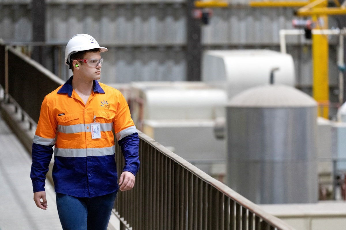 A man wearing a high vis vest and a hard hat walking along a catwalk overlooking a production plant