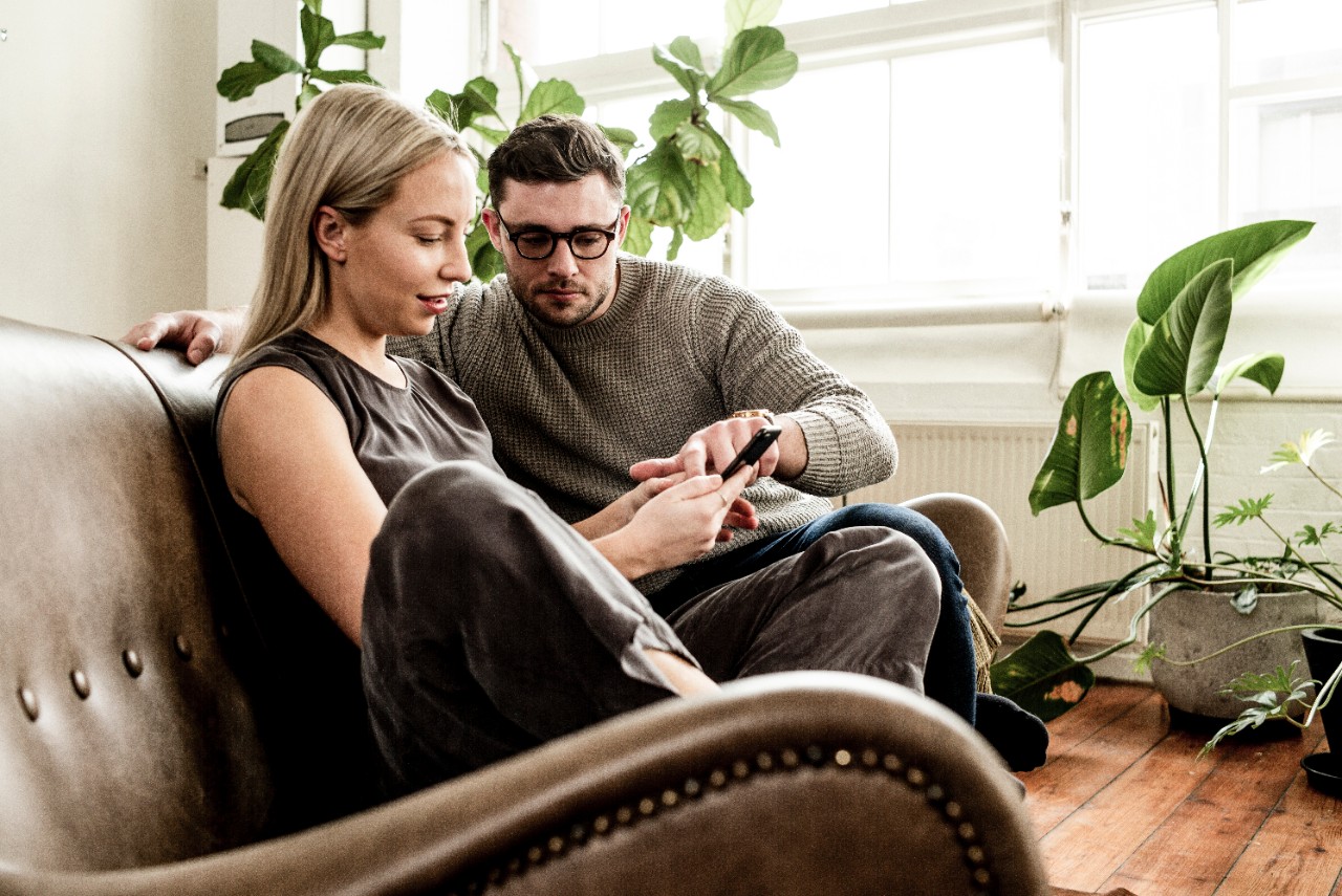 A man and a woman sitting on their couch scrolling on their phone