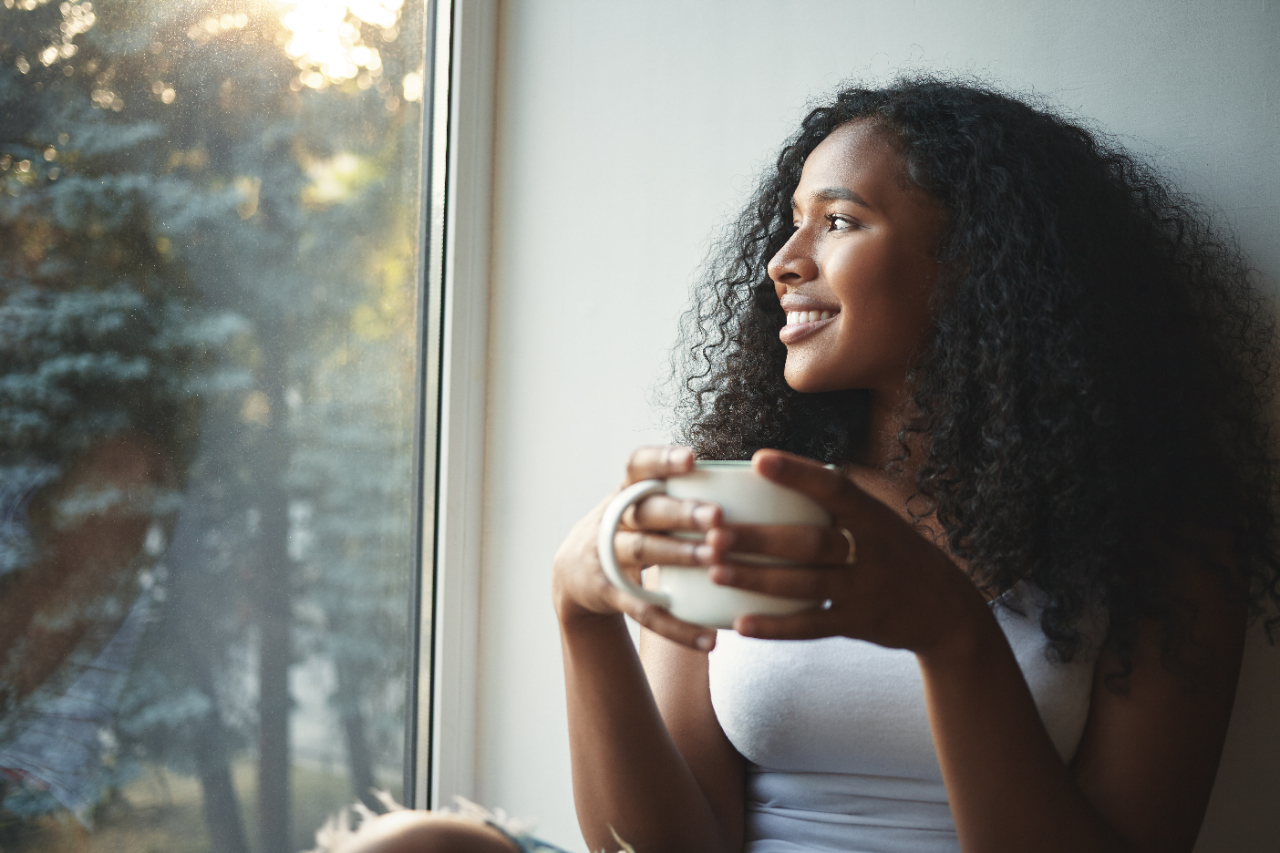Young woman drinking tea and smiling while looking out the window