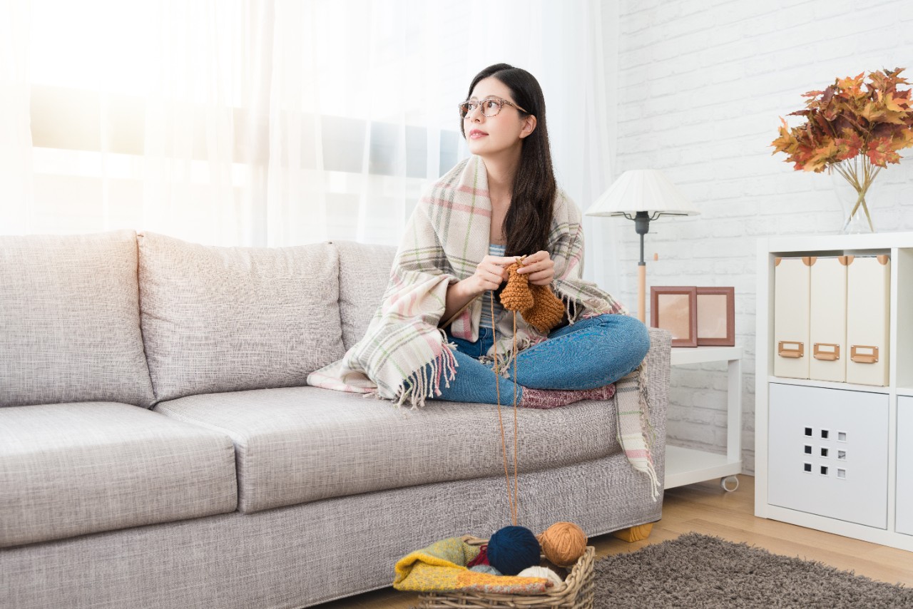 Woman rugged up and knitting on couch