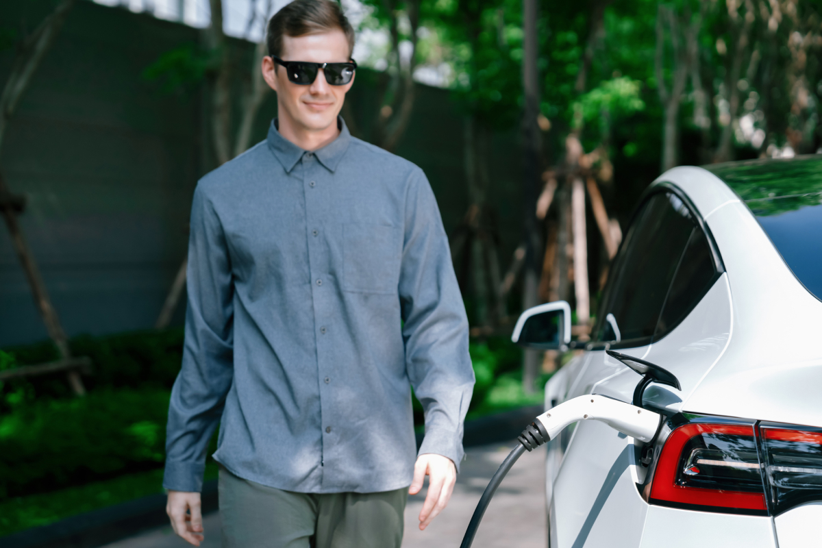 A man stands next to an electric vehicle while it charges